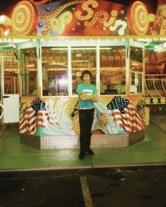 a man standing in front of a carnival ride at night with an american flag on it