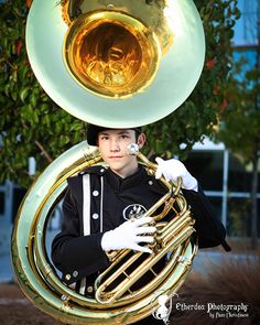 a man in black jacket holding a brass french horn with white gloves on his head