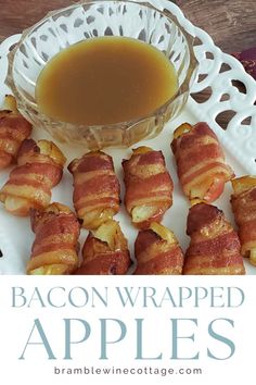 bacon wrapped apples on a white plate next to a bowl of maple syrup and an apple cider