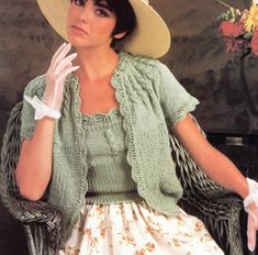 a woman sitting in a chair wearing a white hat and green cardigan sweater with flowers on the wall behind her