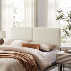 a white bed with pillows and blankets in a bedroom next to a plant on a table