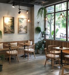 a restaurant with wooden tables and chairs next to large windows that have plants on them