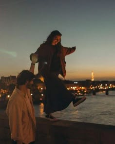 two people standing on a ledge near the water