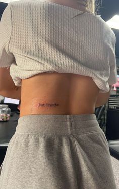 the back of a woman's stomach showing her small tattoo that reads just breathe