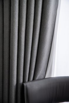 a black leather chair sitting in front of a window covered in gray curtaining and drapes