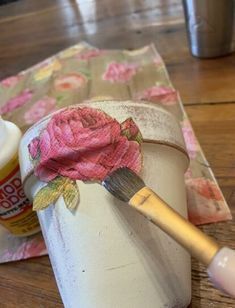 a cup with a flower on it next to a paintbrush and some napkins