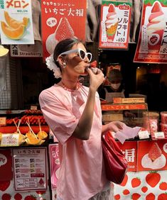 a woman in pink shirt and sunglasses eating an ice cream cone on street corner with orange signs behind her