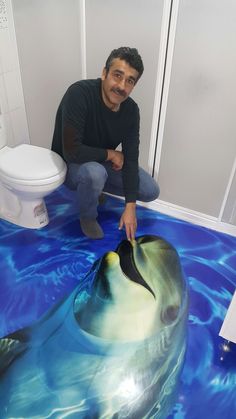 a man kneeling down next to a dolphin painted on the floor in a bathroom with blue water