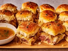 a wooden tray topped with mini sandwiches next to a small bowl of soup and dipping sauce