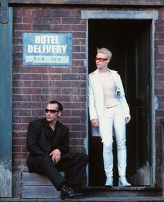 two men sitting on a bench in front of a brick building