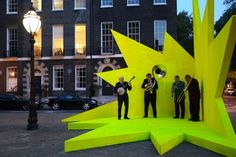 three men are standing in front of a yellow star sculpture with trombones on it