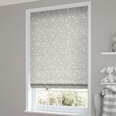 a window with white stars on it in a gray room next to a teddy bear