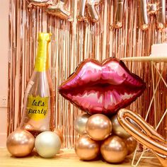 a party decoration with balloons, champagne bottle and lipstick on the table in front of it