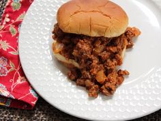 a white plate topped with a sloppy joe sandwich on top of a bun covered in meat