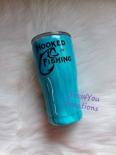 a blue tumbler cup sitting on top of a white fur covered floor with the words hooked to fishing written on it