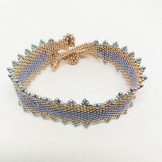 "This stunning handwoven bracelet is featured in gold, galvanized lavender, and galvanized turquoise. Woven bead by bead into place, this bracelet took hours to hand stitch and to get each bead positioned just right. Also features edging, giving this bracelet little points to create a crown like look. The closure is made with beaded balls that a loop of beads from the other side slides over the balls of beads creating a latched effect. The bracelet measure 8.5\"." Metal Beaded Bracelets With Gold Beads, Gold Beaded Metal Bracelets, Metal Beaded Bracelets With Spacer Beads As Gift, Gold Jewelry Spacer Beads For Crafting, Metal Bracelet With Gold Beads, Bohemian Gold Friendship Bracelets With Spacer Beads, Gold Beaded Braided Bracelets In Bohemian Style, Gold Bohemian Friendship Bracelets With Spacer Beads, Gold Beads Metal Bracelet