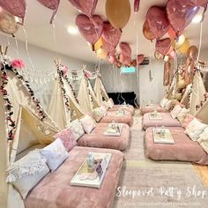 a room filled with lots of pink beds covered in pillows and balloons hanging from the ceiling