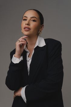 a woman in a black suit and white shirt is posing for the camera with her hand on her chin