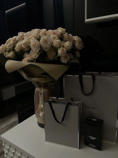 a bouquet of white roses sitting on top of a table next to two small bags