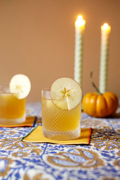 two glasses filled with drinks sitting on top of a table next to candles and pumpkins