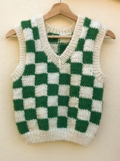 a green and white knitted sweater hanging on a wooden hanger next to a wall