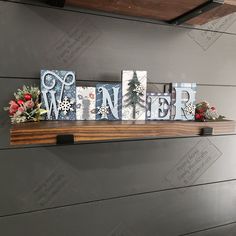 a wooden sign that says winter with snowflakes and evergreens on it in front of a gray wall