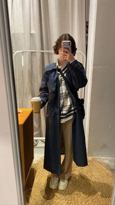 a person taking a selfie in front of a mirror wearing a trench coat and khaki pants