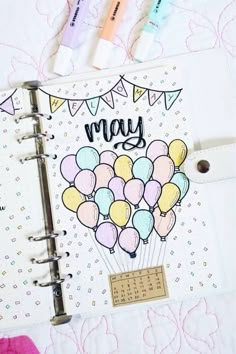 an open planner with balloons on it and the words may written in black ink next to some markers