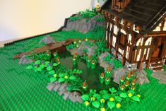 a house made out of legos sitting on top of a green field next to a pond