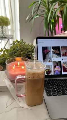 a laptop computer sitting on top of a table next to a cup of coffee and a candle