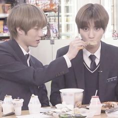 two young men sitting at a table eating food