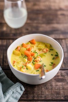 a white bowl filled with soup next to a glass of water on top of a wooden table