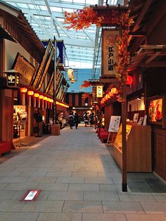 an empty shopping mall with people walking down the walkway and shops on both sides, under a glass ceiling