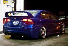 the back end of a blue car parked at a gas station in front of a gas pump