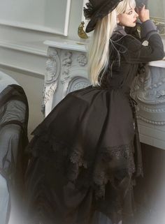 a woman in a black dress and hat sitting at a table with her hand on her head