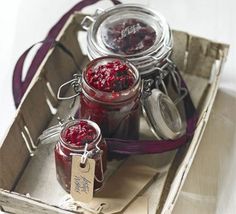 three jars of raspberry jam sit in a wooden crate with tags on them