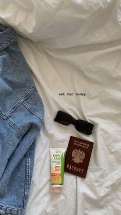 the contents of a travel bag laid out on top of a white bed with a passport, sunglasses and eyeglasses