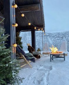 an outdoor fireplace in the middle of a snowy area with chairs and lights on it