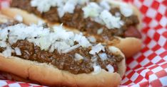 two chili cheese dogs with onions and ketchup in a red and white checkered paper basket