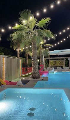 an outdoor swimming pool at night with palm trees and lights strung over the poolside