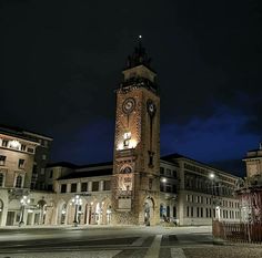 a clock tower lit up at night in the middle of a town square with cobblestone streets