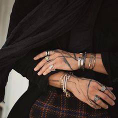 a woman with tattoos on her arms and hands wearing rings, bracelets and scarves