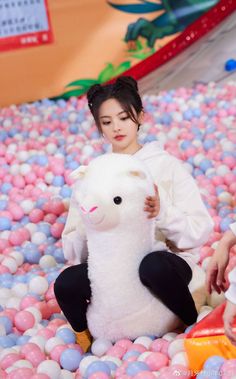 a woman sitting on top of a ball pit holding a stuffed animal in her hands