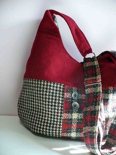 a red and black plaid purse sitting on top of a white table next to a wall