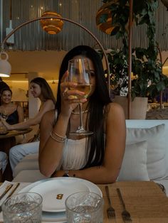 a woman sitting at a table with a glass of wine in front of her face