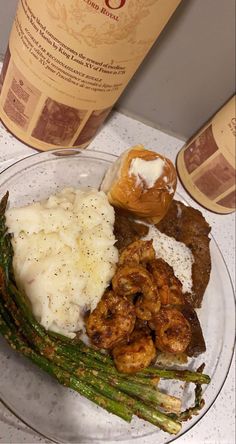 a plate with mashed potatoes, asparagus and shrimp next to a bottle of wine