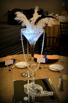 a tall glass vase filled with pearls and feathers on top of a table next to plates