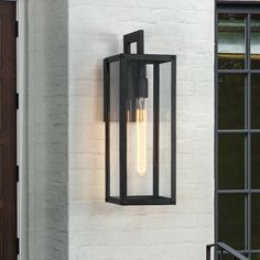 Illuminate your front door or garage with this contemporary exterior wall mounted lantern light. It's rated for wet locations, and its sleek frames are made from metal in a powder-coated black finish that complements your decor from classic to rustic. It features 4 clear glass panels with a elongated shape enclosed in a black and sleek clean-lined framework. E26 long tubular bulb is recommended to fully illuminate the glass and to complement the overall aesthetic, or use a Edison bulb to enhance a vintage look. It's Ideal for Front Porch, Patio, Garage, Deck etc. Plus, it's compatible with a dimmer switch, so you can make the most out of your lighting. True Fine Spun 1-Light 18.5-in H Matte Black LED Outdoor Wall Light | TD130013OT Black Outdoor Lights, Porch Light Fixtures, Front Porch Lighting, Outdoor Wall Light Fixtures, Wall Mount Lantern, Modern Lanterns, Exterior Light Fixtures, Black Outdoor Wall Lights, Contemporary Exterior