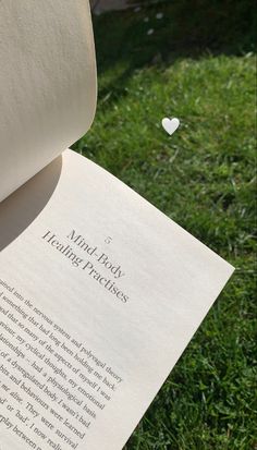 an open book sitting on top of a lush green field next to a white heart