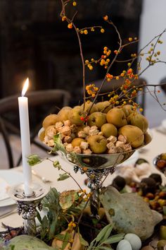 an arrangement of fruit and flowers on a table with a candle in the centerpiece